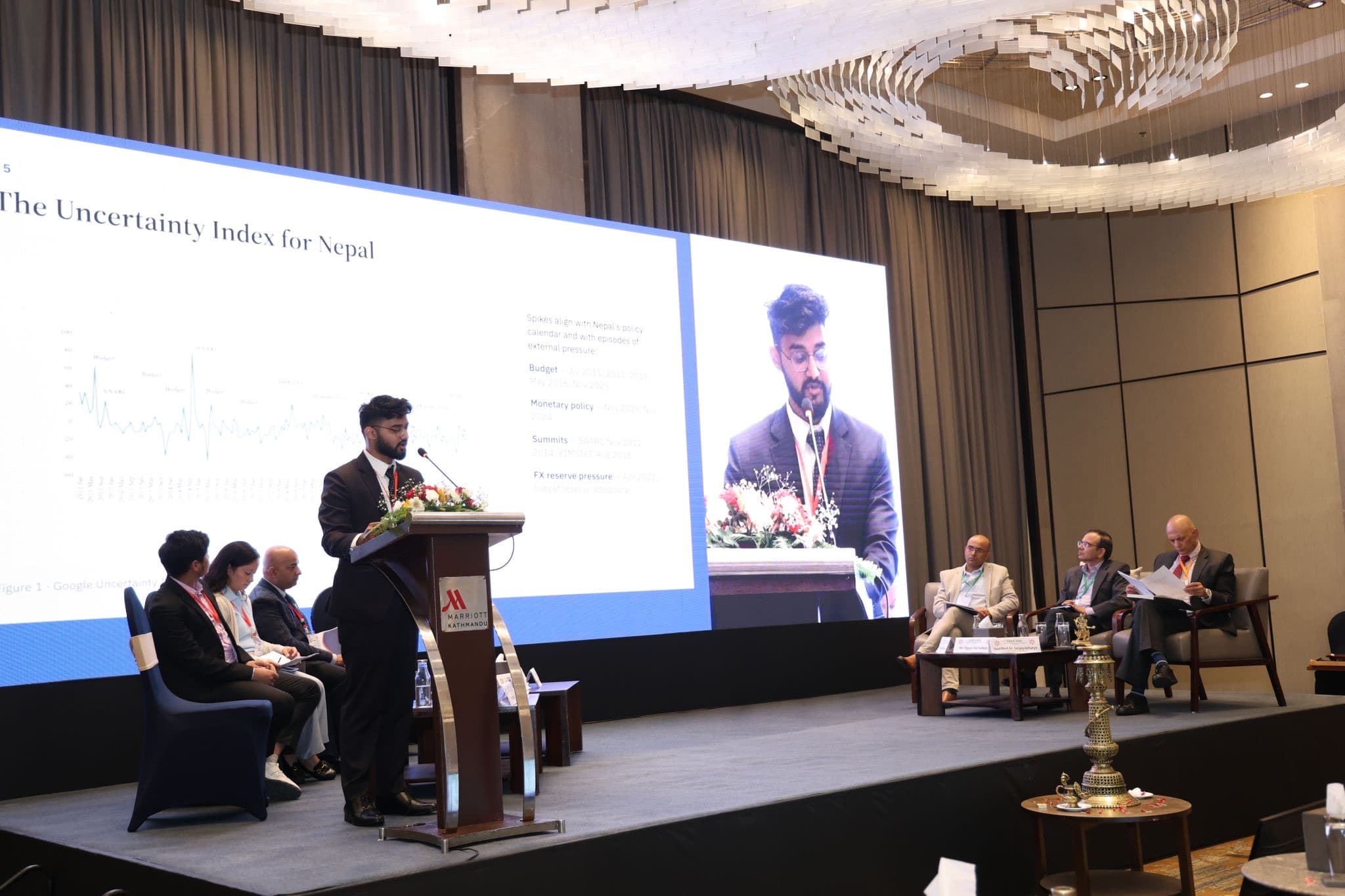 Swostik Nepal presenting the Economic Policy Uncertainty index for Nepal on stage at CAICE 2026, with the slide on the main screen
